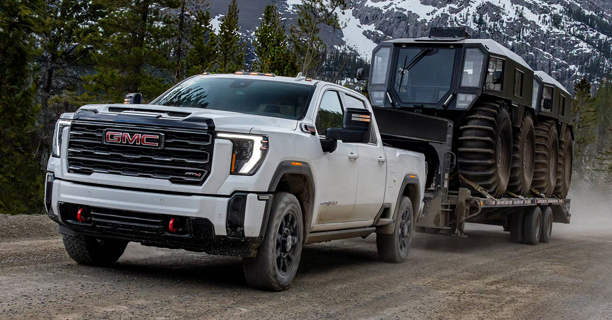 A white 2026 GMC Sierra HD hauling heavy equipment